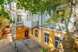 A courtyard with a yellow building, a staircase, and a tree.