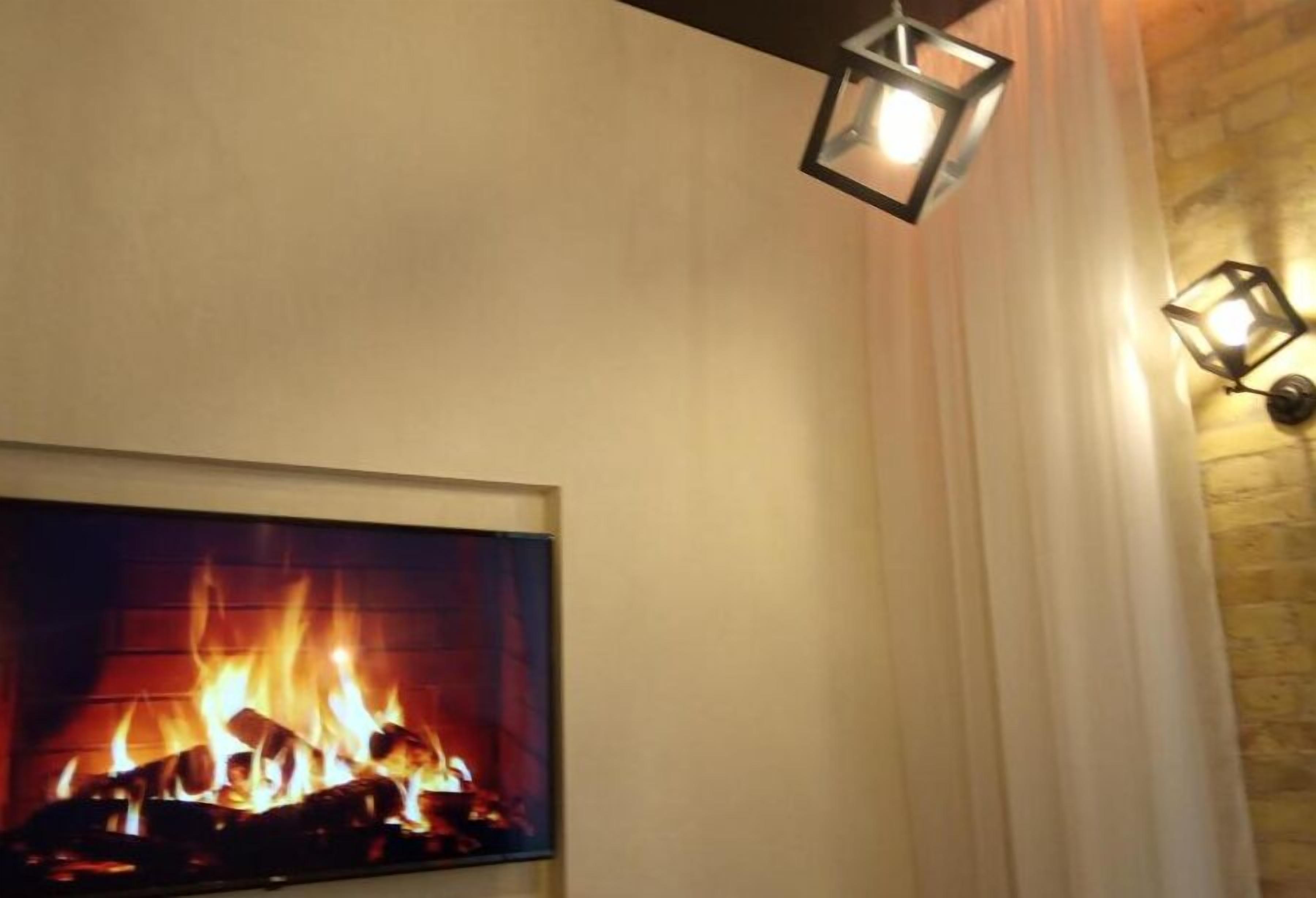 A fireplace with a fire, a white curtain, and a brick wall.