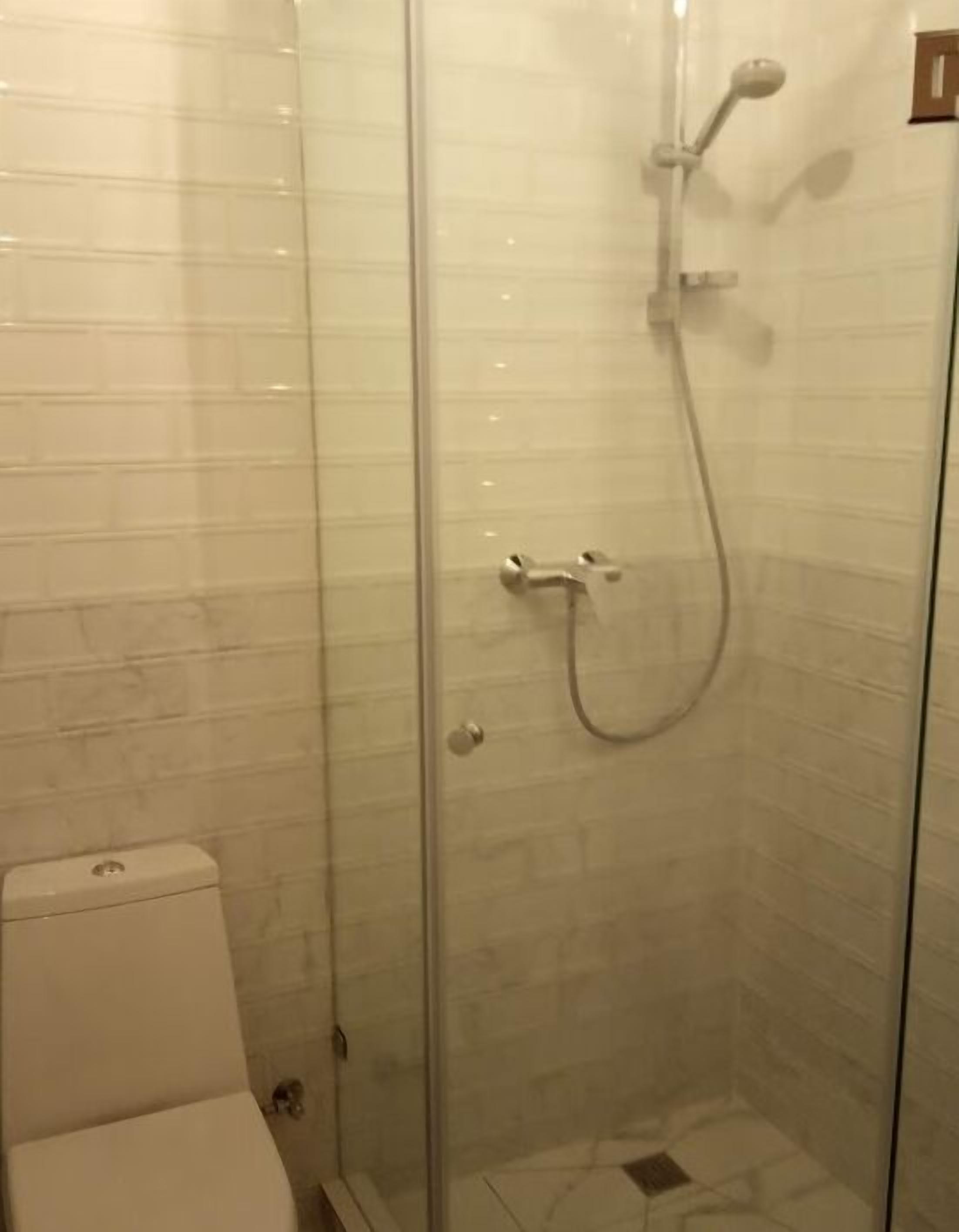 Un box de ducha con paredes de vidrio, un cabezal de ducha de mano y un grifo instalado en la pared.