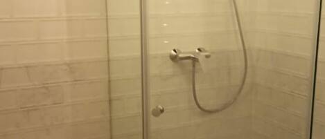 Un box de ducha con paredes de vidrio, un cabezal de ducha de mano y un grifo instalado en la pared.