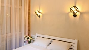 Una cama bien hecha con sábanas blancas y dos toallas negras, una mesita de noche y una lámpara de pared.