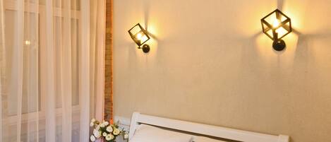 A neatly made bed with white linens and two black towels, a bedside table, and a wall-mounted light fixture.