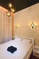 A neatly made bed with white linens and two black towels, a bedside table, and a wall-mounted light fixture.