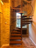 A spiral staircase with wooden steps and metal railings, leading to an upper floor.