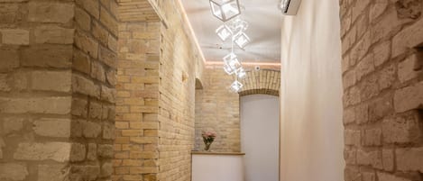 A narrow hallway with exposed brick walls, a white reception desk, and a hanging light fixture.