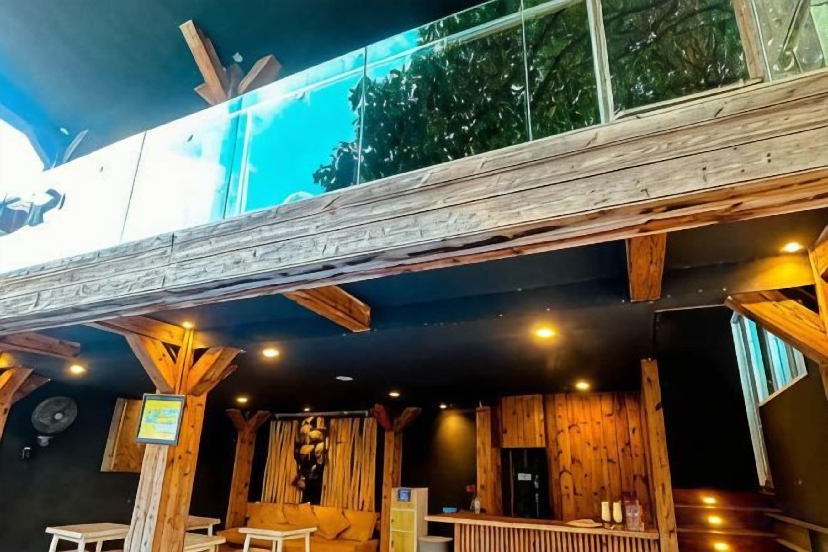 Een houten interieur met een hoge plafond en zichtbare balken, met een bargedeelte met krukken en een bar.