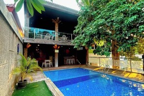 A swimming pool with a glass balustrade, surrounded by potted plants and a tree. - De Baghraf by Amithya (Sumenep)