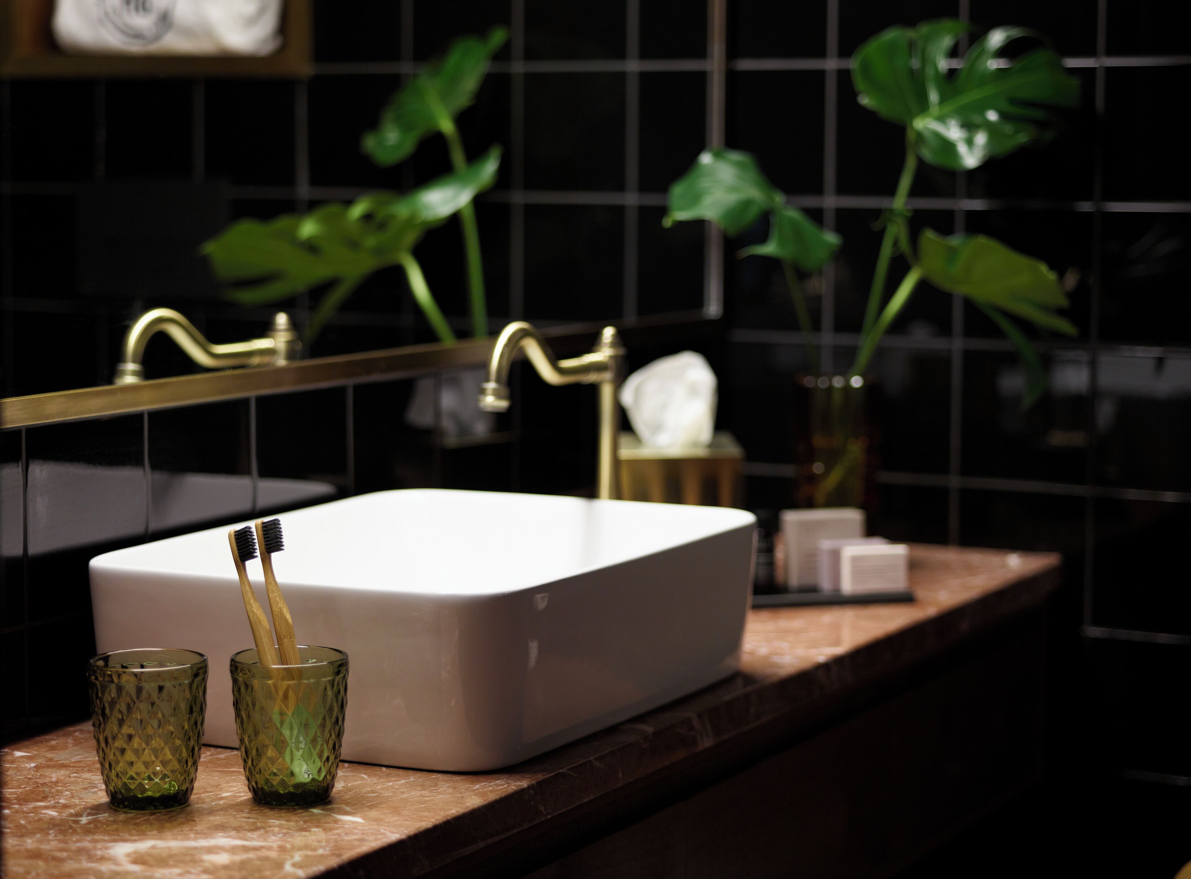 Ein Badezimmer mit einem weißen Waschbecken, zwei grünen Gläsern und einer Zahnbürste.