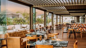 A spacious restaurant with a terrace overlooking a cityscape, featuring wooden tables and chairs, and a view of a mountain. - Brown Acropol, a member of Brown Hotels (Athens)