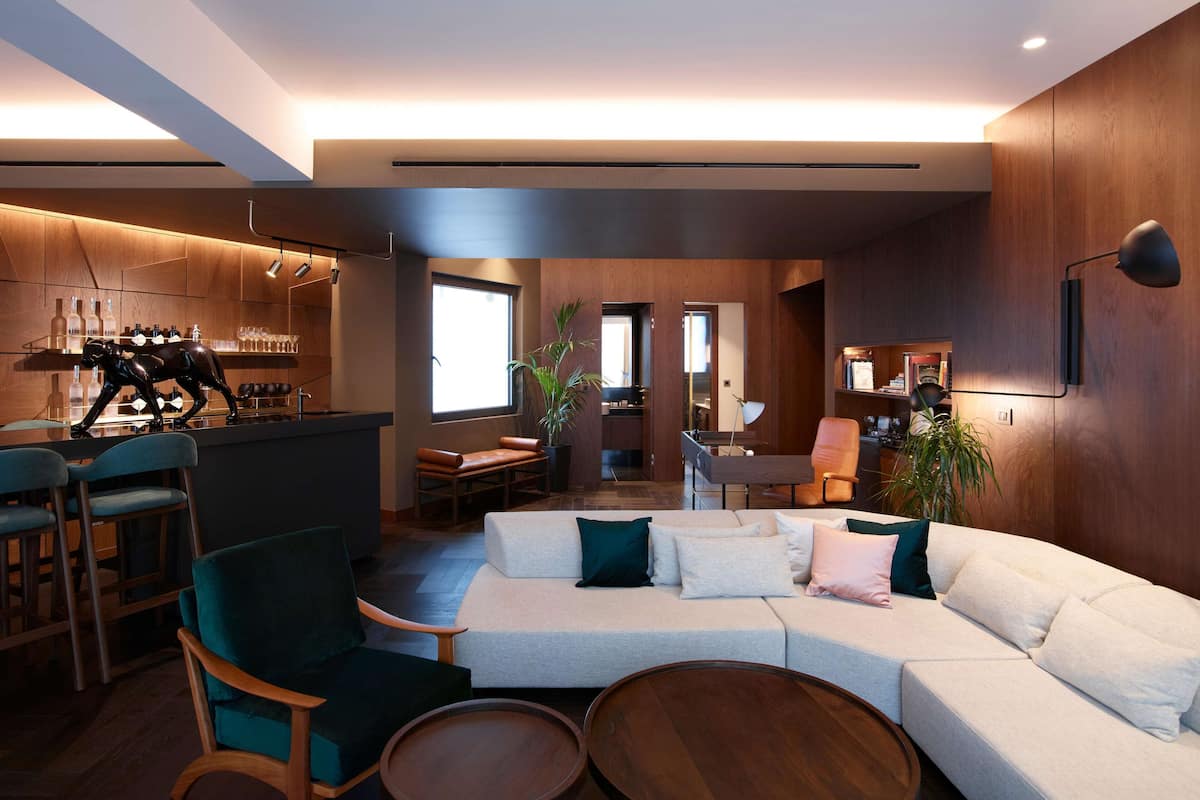 Uma sala de estar moderna com um sofá branco, cadeiras verde-água e uma mesa de centro de madeira. Uma cozinha com armários de madeira e um balcão é visível ao fundo.