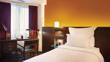 A hotel room with a bed, a desk with a chair, a telephone, and a nightstand with a lamp.