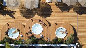 A rooftop pool area with three hot tubs, surrounded by wooden decking and covered with woven umbrellas. - Brown Acropol, a member of Brown Hotels (Athens)
