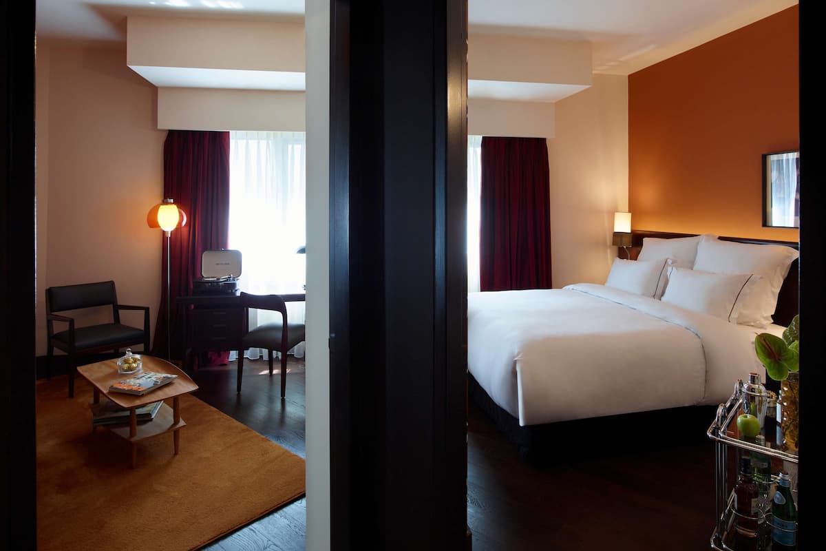 Quarto de hotel com cama, escrivaninha com computador, cadeira e uma mesinha com uma revista.