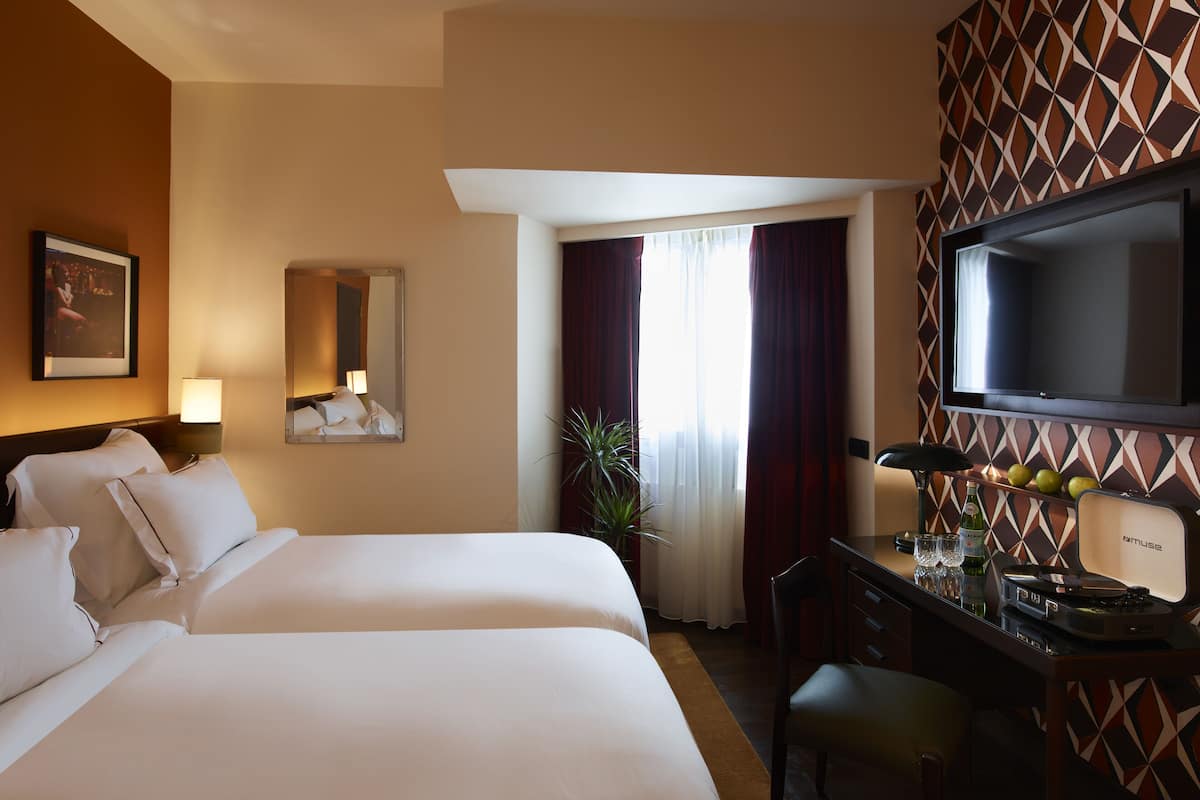 Quarto de hotel com duas camas, uma escrivaninha com computador, televisão e minibar.