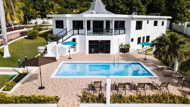 Um edifício moderno de dois andares com piscina, área de estar ao ar livre e vegetação exuberante.