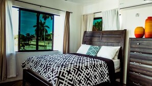 Quarto com cama, penteadeira e janela com vista para um jardim.