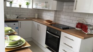Una cuina moderna amb armaris blancs, forn negre i tetera vermella al taulell.