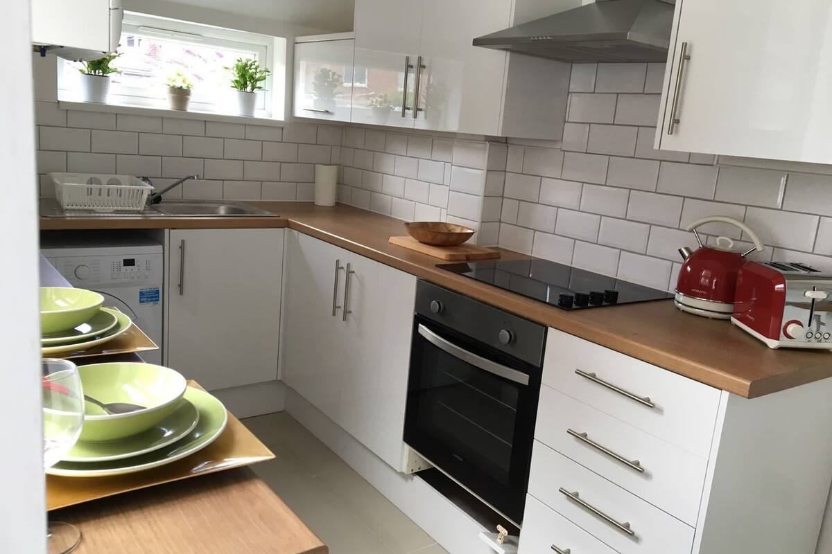 A modern kitchen with white cabinets, a black oven, and a red kettle on the countertop.