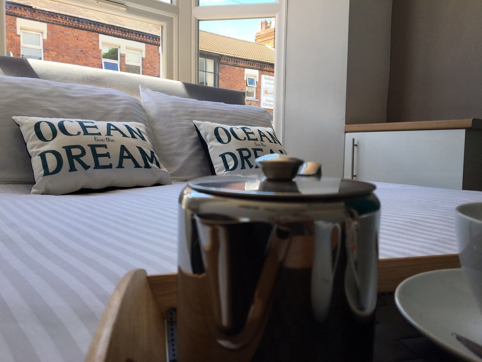 En säng med kuddar som har texten ”HAVSDrÖM” på sig, och en kaffekanna på ett brickbord.