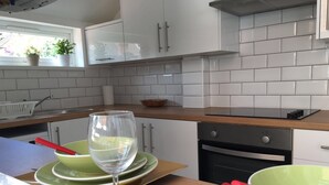 Una cuina moderna amb armaris blancs, taulell de fusta i una finestra amb plantes.