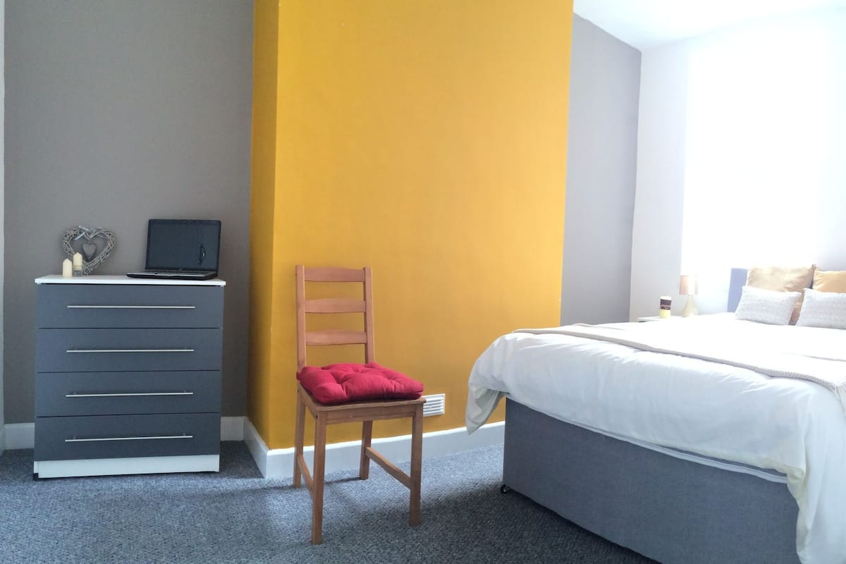 A bedroom with a bed, a desk with a laptop, a chair, and a dresser.