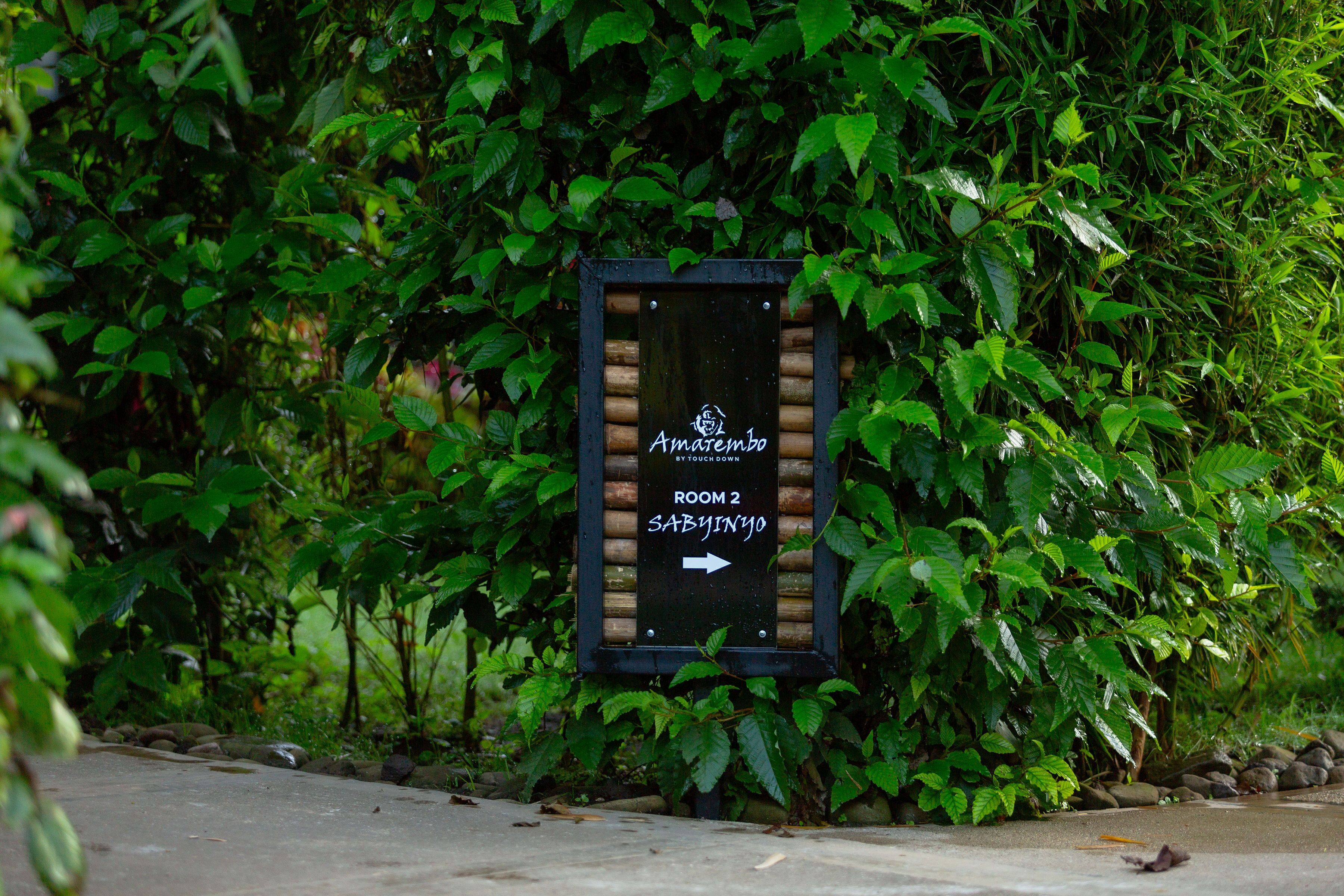 A signboard with a wooden frame, indicating 'Amate inbo ROOM 2 SABYINYO' with an arrow pointing to the right.