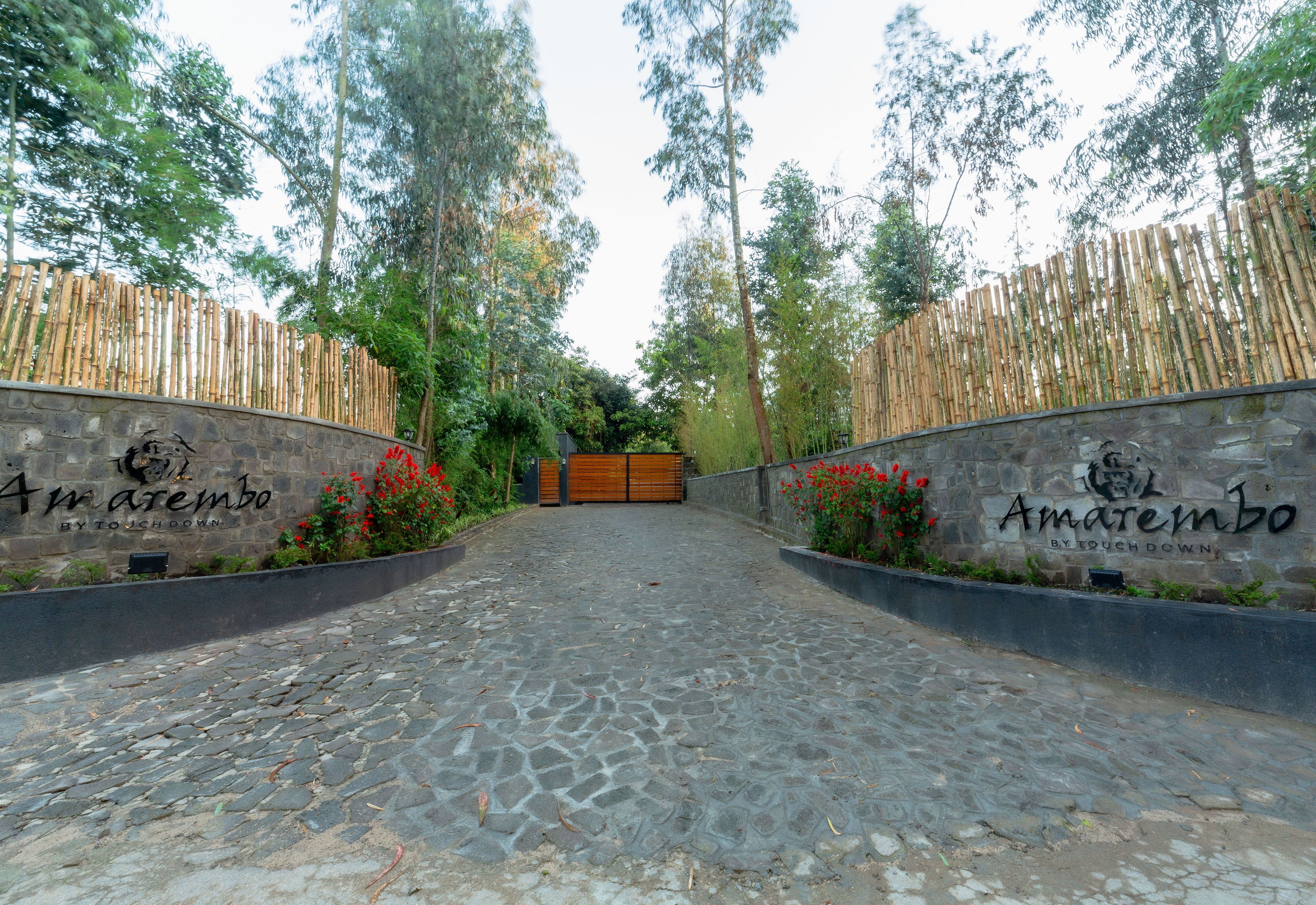 A cobblestone pathway leading to a wooden gate, flanked by bamboo fences and stone walls with the name "Amaremba" visible.