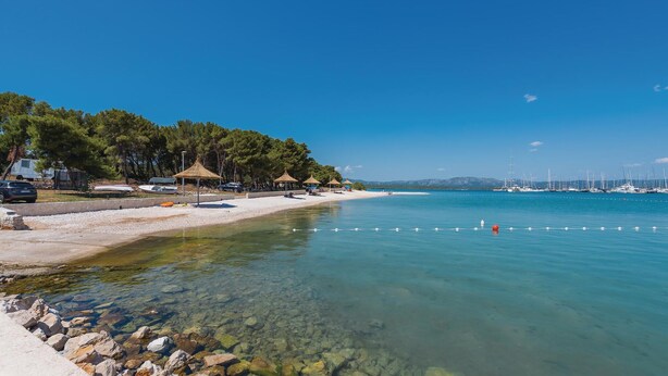 A beach with clear water, a row of beach umbrellas, and a marina in the background. - Luxurious home in Betina (Betina)