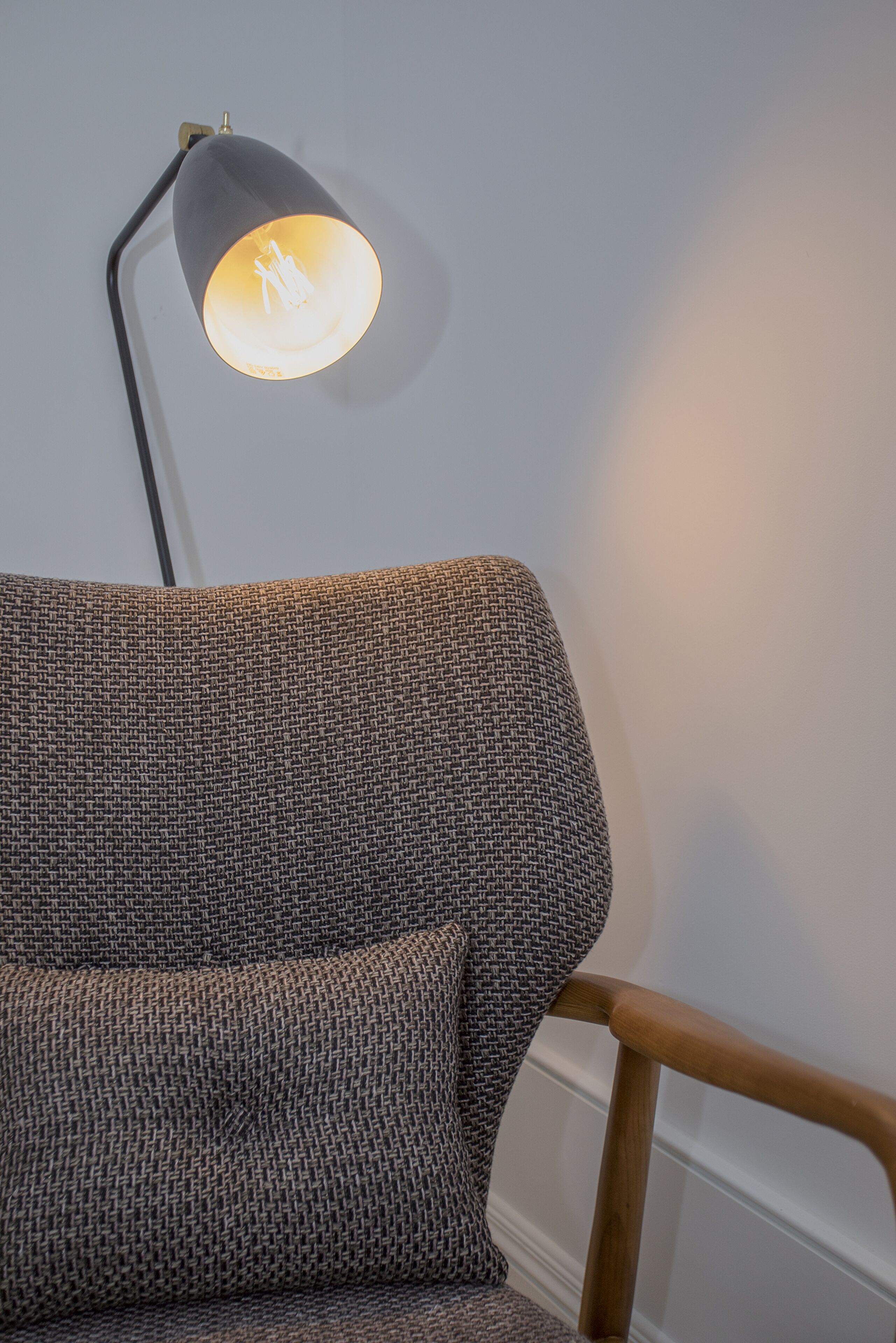 A corner of a room with a grey patterned sofa and a wooden chair.