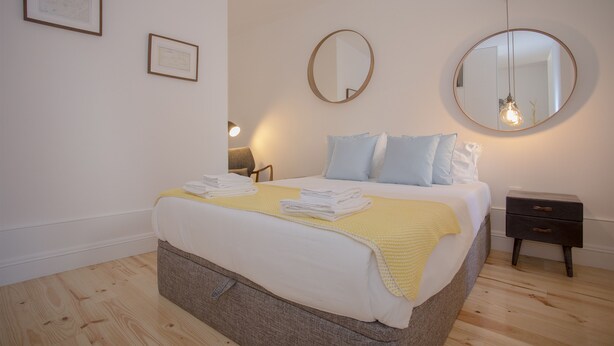 A neatly made bed with a yellow blanket, two bedside tables, and two framed pictures on the wall. - Liiiving - Clérigos Terrace Apartment (Porto)