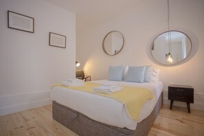 Un lit bien fait, recouvert d’une couverture jaune, deux tables de chevet et deux tableaux encadrés accrochés au mur.