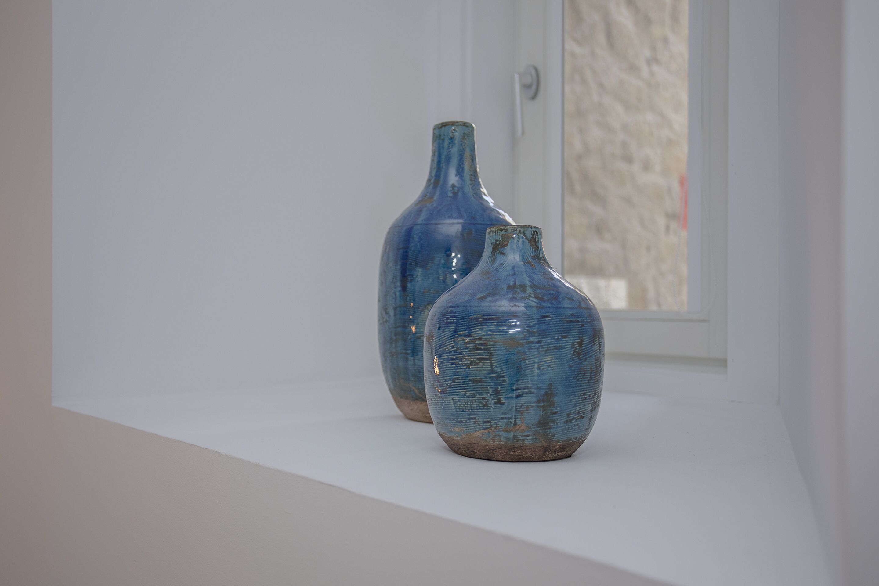 Two blue vases on a white shelf by a window.