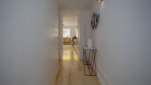 A hallway with wooden flooring, a white wall, and a small table with a vase. - Liiiving - Clérigos Terrace Apartment (Porto)