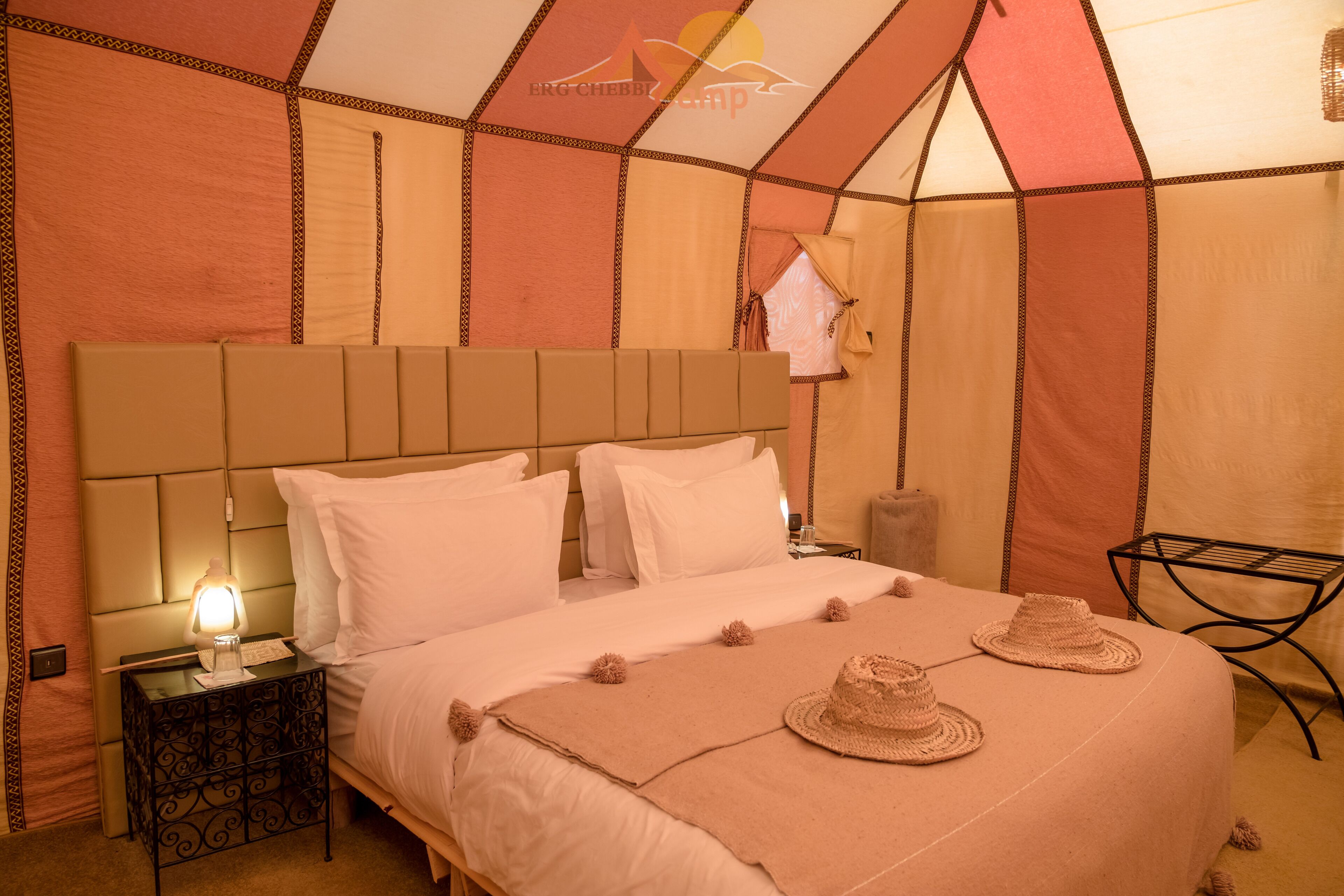 A tent-style bedroom with a bed, pillows, a nightstand, and a lamp.