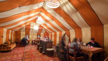 A tented dining area with tables, chairs, and a chandelier.