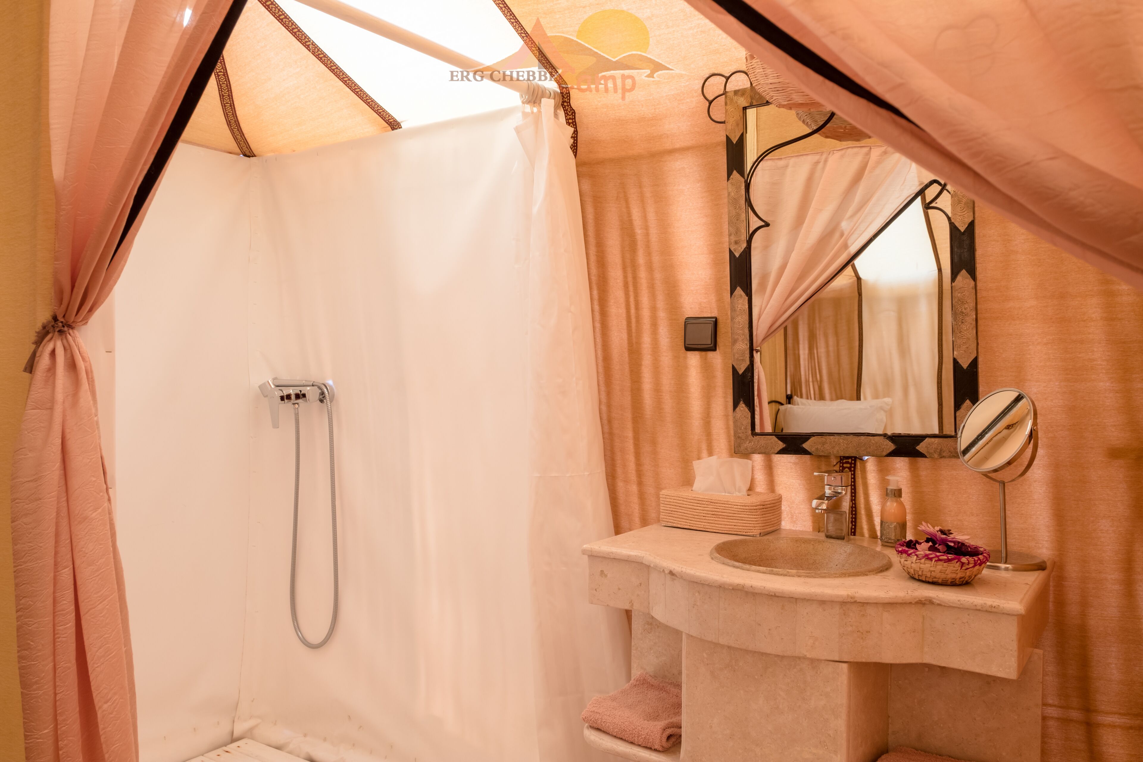 A tented bathroom with a shower, sink, and mirror.