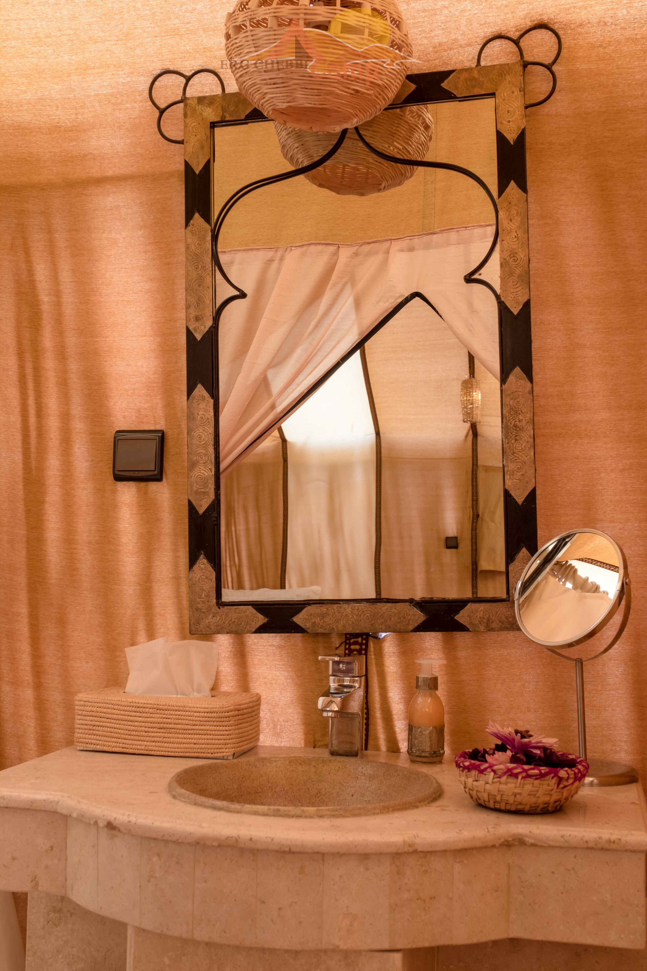 Une salle de bain avec un grand miroir, un lavabo, une boîte de mouchoirs et un panier décoratif.