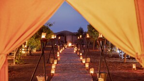 A tented area with a carpeted walkway lined with candles, leading to a central fire. - Erg Chebbi Camp (Taouz)