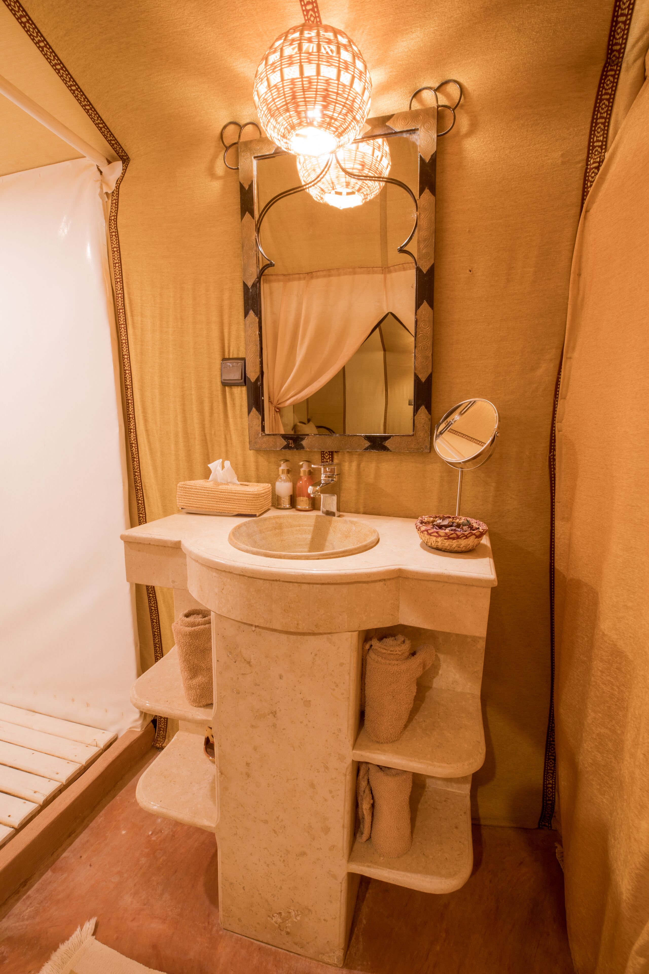 Un baño con un lavamanos color beige, un espejo, un perchero para toallas y una lámpara colgante.