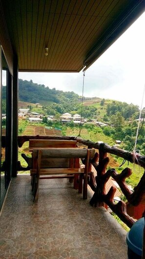 A covered outdoor area with a wooden bench and a view of a village. - Phu Fa Sai Homestay (Mae Rim)