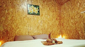A room with a wooden wall, a bed with white bedding, a brown pillow, and a picture of flowers on the wall. - Phu Fa Sai Homestay (Mae Rim)