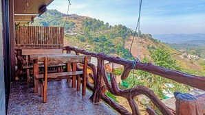 A wooden outdoor seating area with a table and benches, overlooking a hilly landscape with houses. - Phu Fa Sai Homestay (Mae Rim)