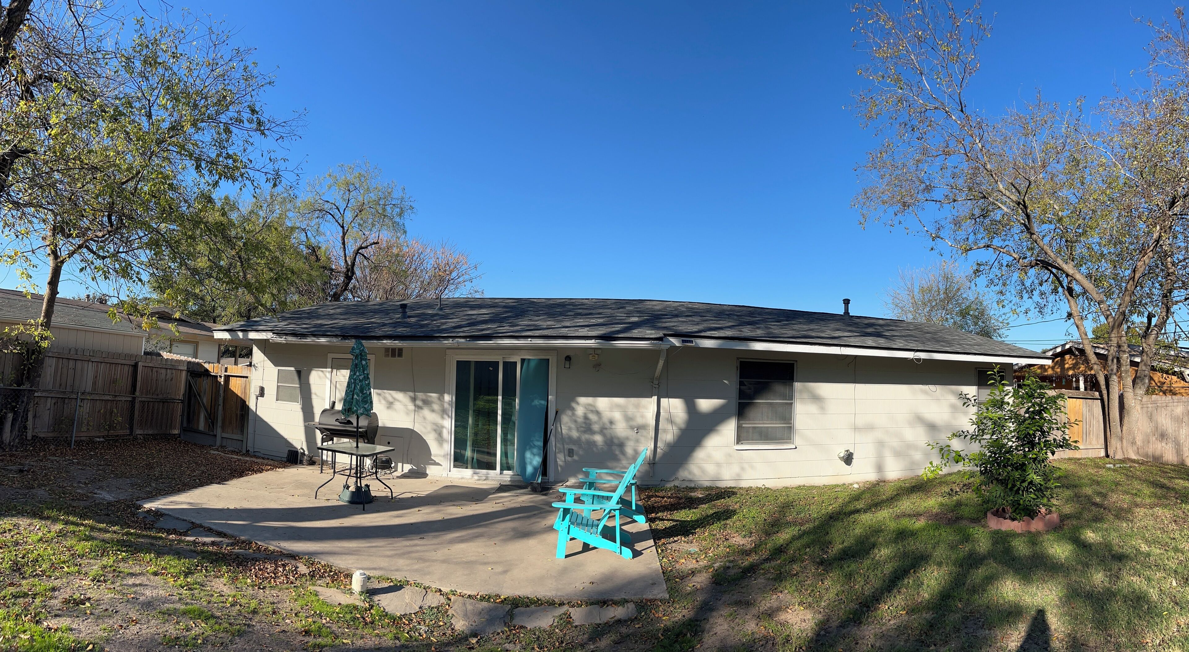 A single-story house with a covered patio, a barbecue grill, and a small tree in the yard.