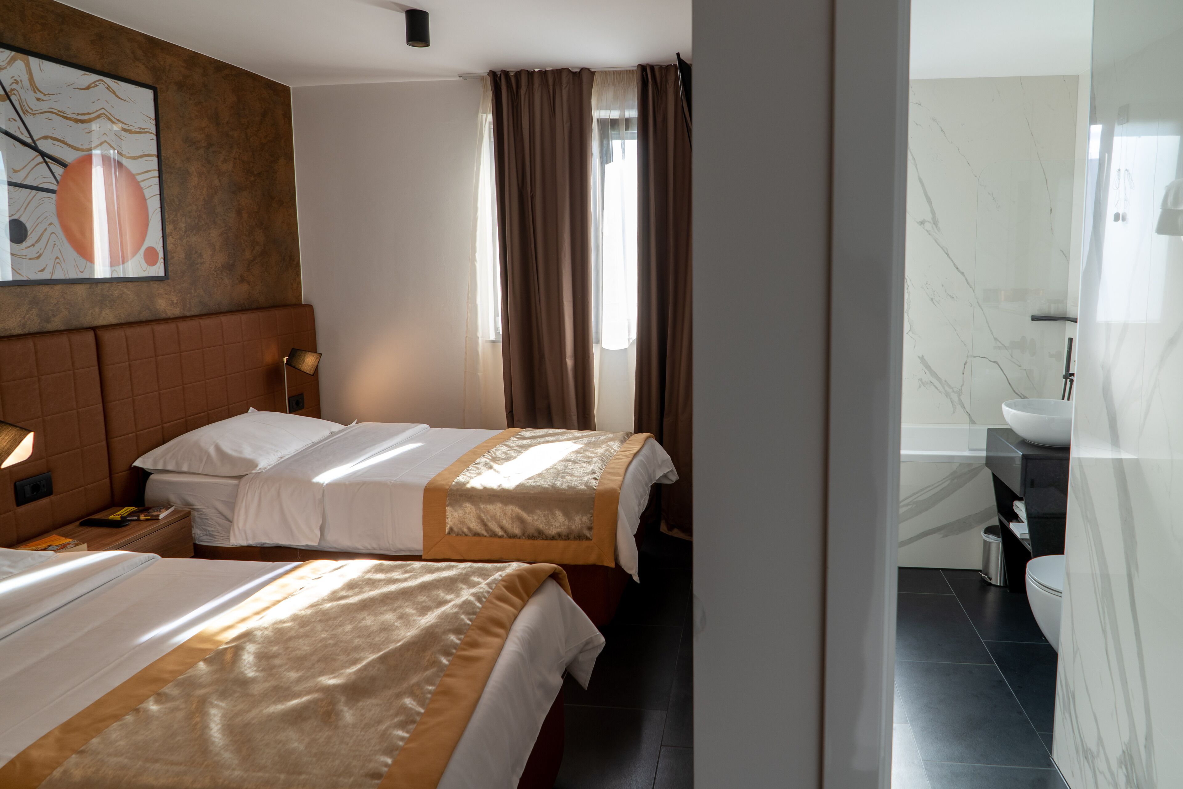 Une chambre d’hôtel avec deux lits, une salle de bain avec un lavabo blanc et une grande fenêtre avec des rideaux.