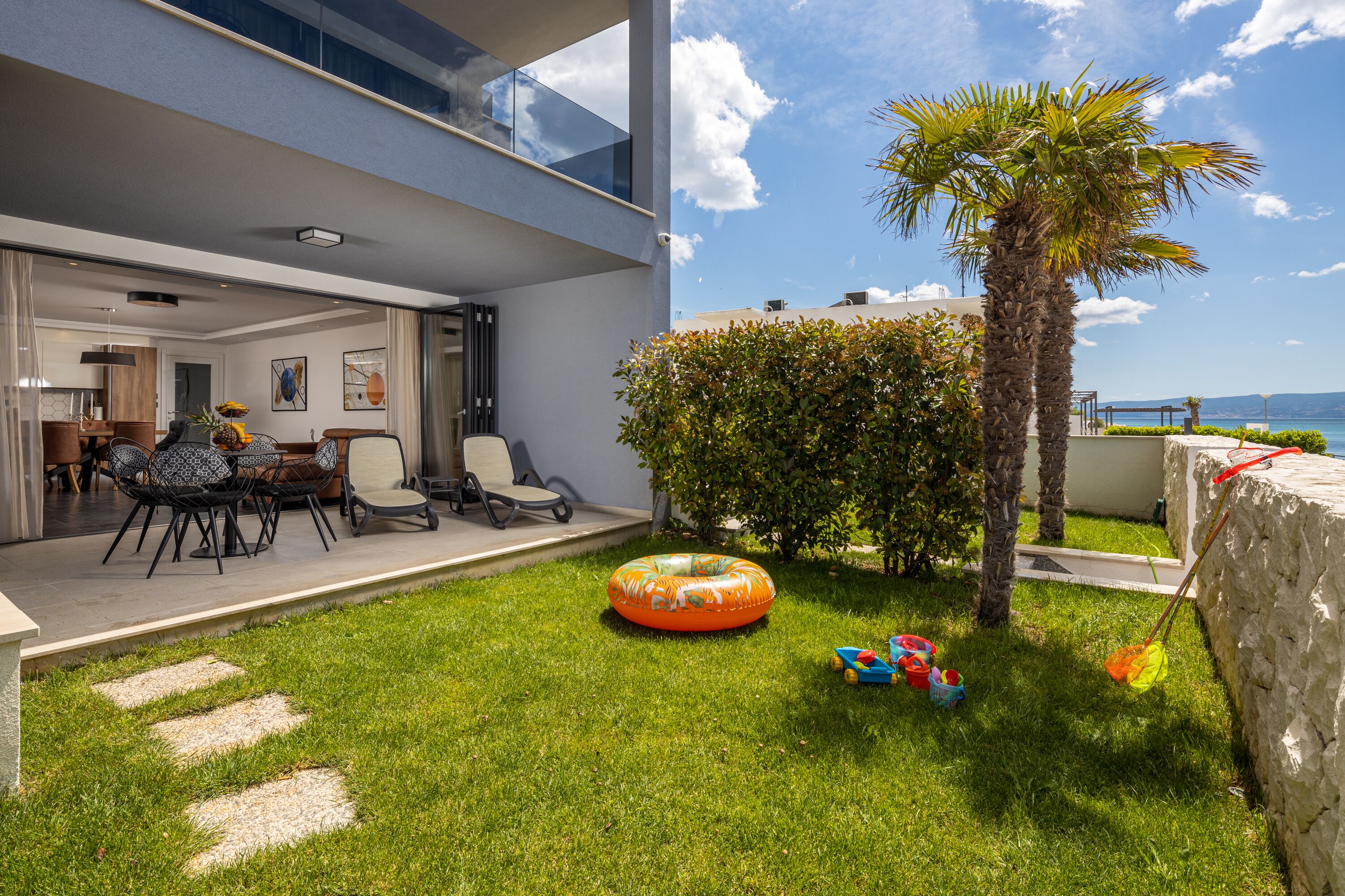 Eine moderne Terrassenanlage im Freien mit Essbereich, einer Palme und Blick auf das Meer.