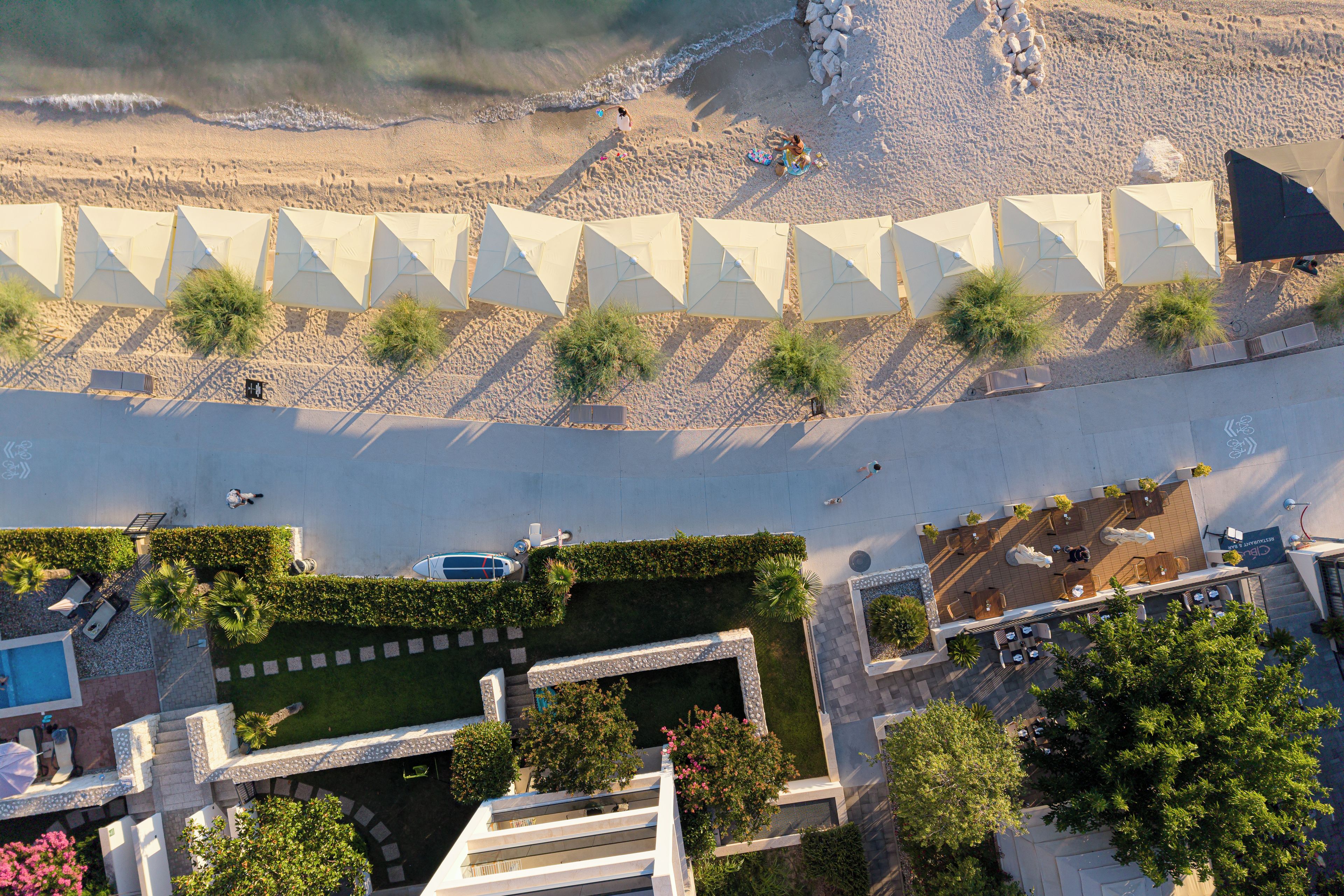 An aerial view of a resort with multiple beach umbrellas, a pool area, and a landscaped garden.
