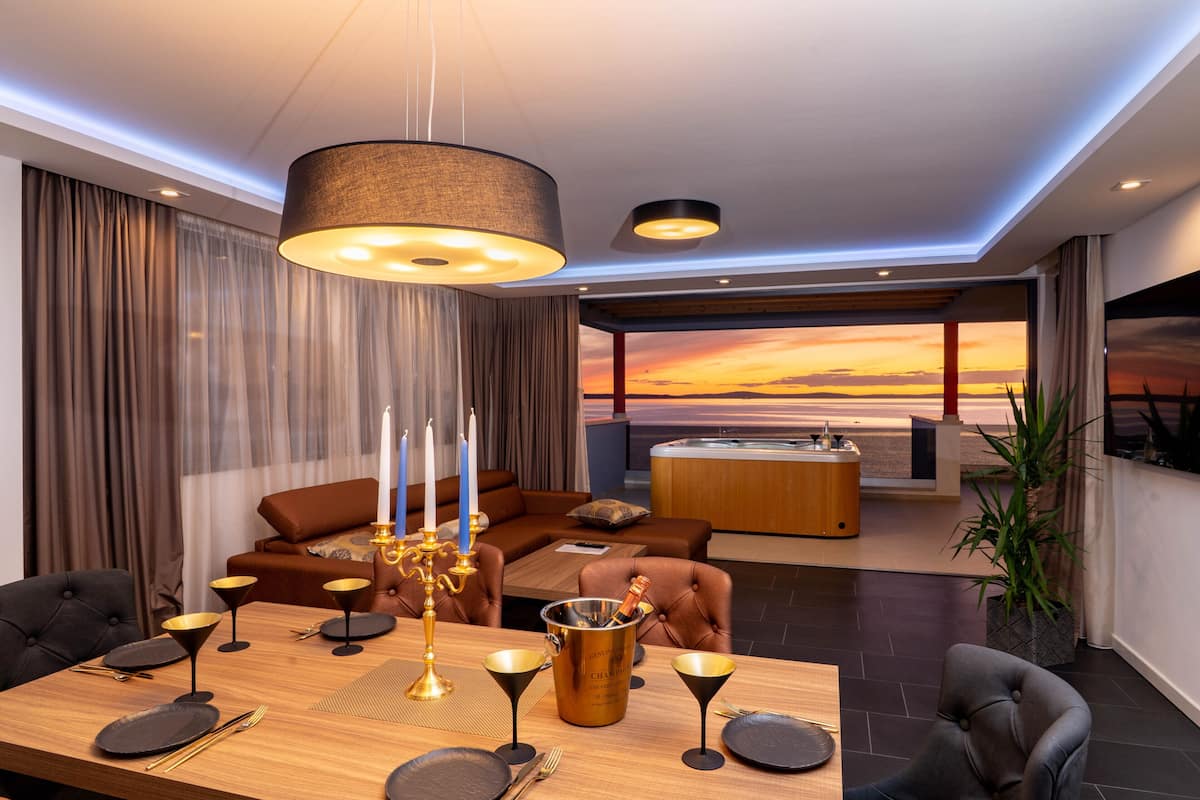 A modern living room with a dining area, a large window with a sunset view, a fireplace, and a cozy seating arrangement.