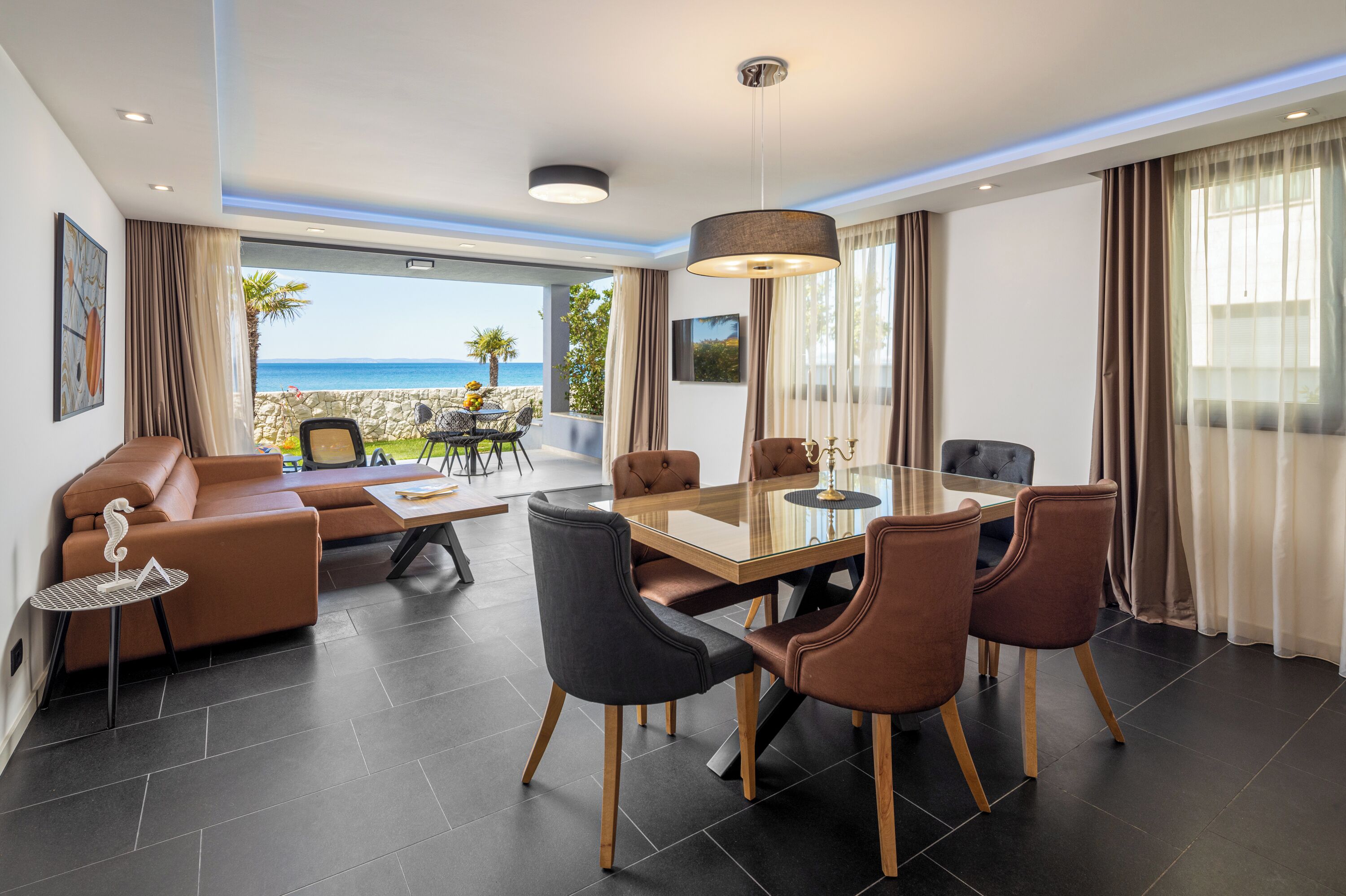 A modern interior with a dining area, seating, and a view of the sea.