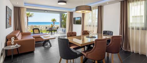 A modern interior with a dining area, seating, and a view of the sea.