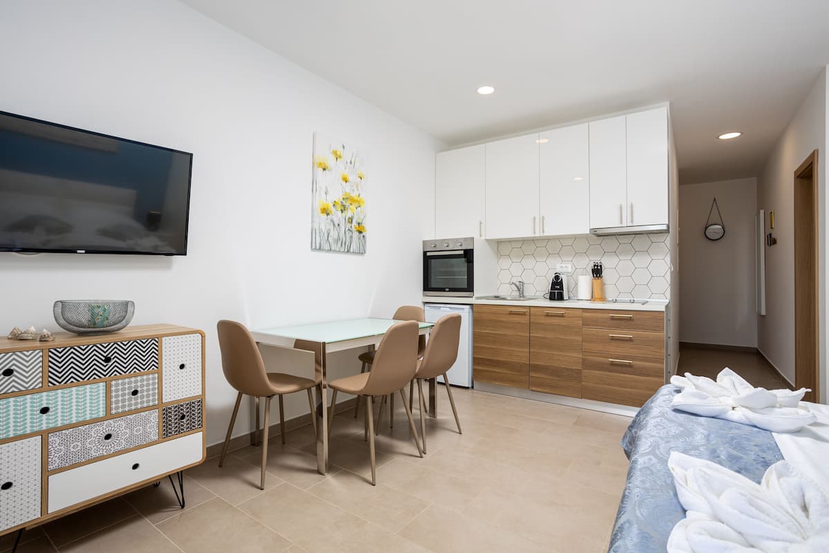 A modern hotel room with a dining area, kitchenette, and a TV mounted on the wall.